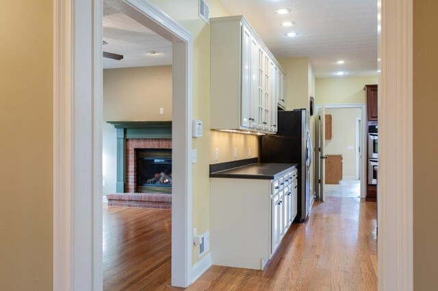 kitchen featuring white cabinetry, a fireplace, appliances with stainless steel finishes, and light wood-type flooring