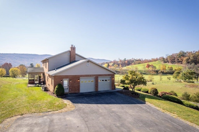 view of side of home with cooling unit, a garage, a yard, a mountain view, and a rural view