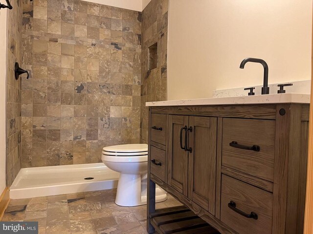 bathroom featuring a tile shower, vanity, and toilet