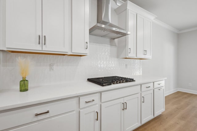 kitchen with wall chimney range hood, light wood-type flooring, ornamental molding, stainless steel gas stovetop, and white cabinets