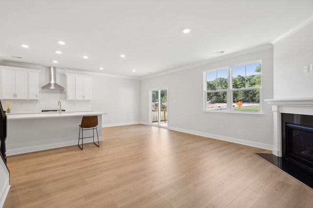 living area featuring visible vents, a glass covered fireplace, light wood-style floors, crown molding, and baseboards