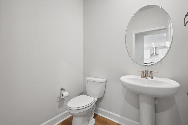 half bath with a sink, baseboards, toilet, and wood finished floors