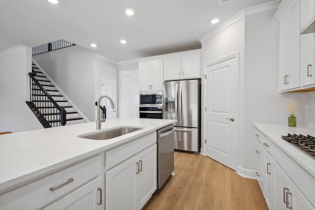 kitchen with light wood finished floors, ornamental molding, stainless steel appliances, white cabinetry, and a sink