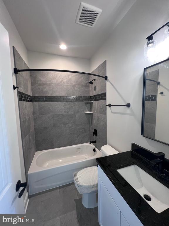 full bathroom with tiled shower / bath, vanity, and toilet