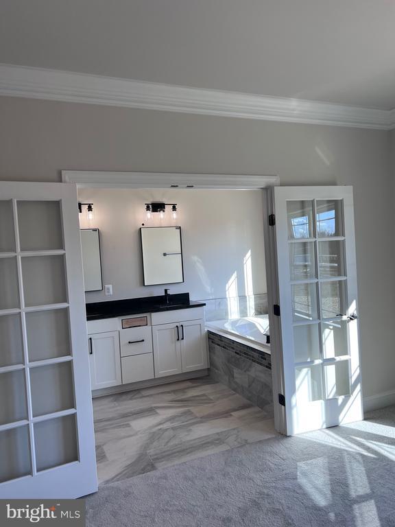 bathroom with a relaxing tiled tub, vanity, and crown molding