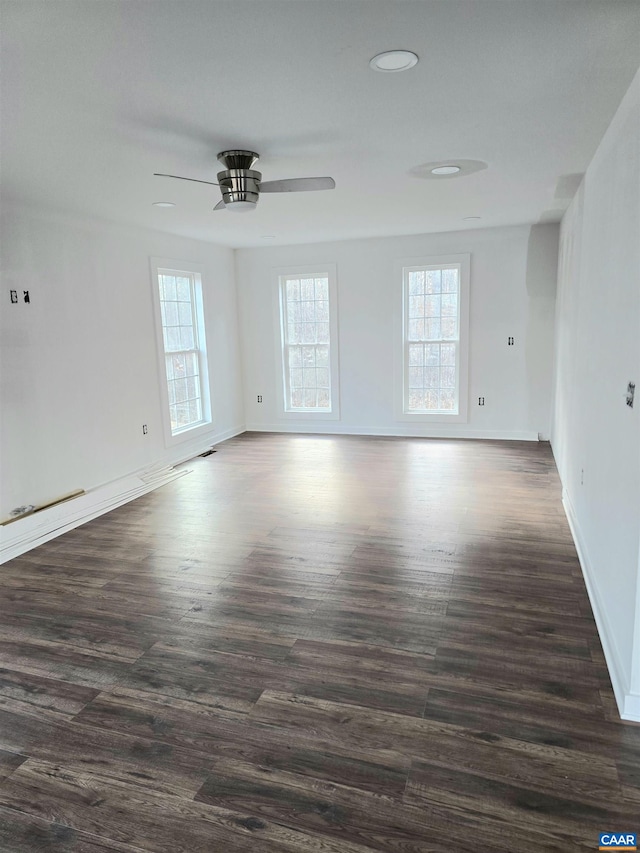 empty room with ceiling fan, a healthy amount of sunlight, and dark hardwood / wood-style flooring