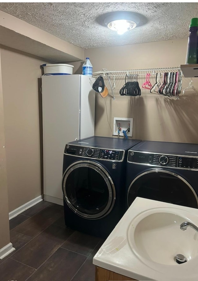 laundry room featuring washing machine and clothes dryer, dark tile patterned floors, laundry area, a textured ceiling, and a sink