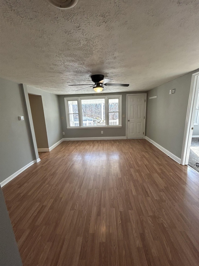 unfurnished living room with a textured ceiling, dark wood-type flooring, and baseboards