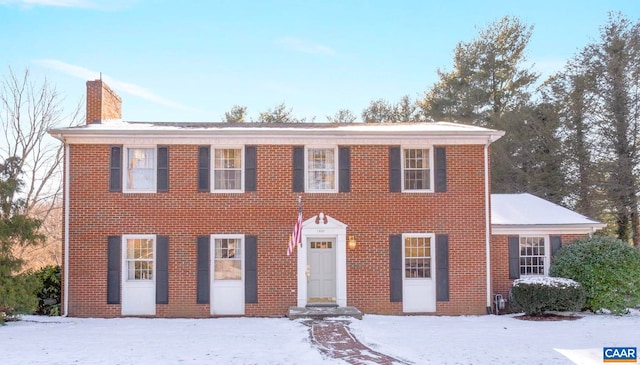 colonial home featuring a chimney and brick siding