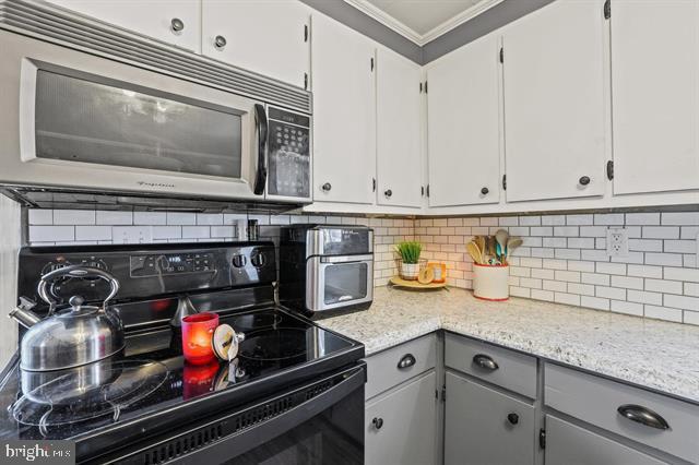 kitchen featuring electric range, decorative backsplash, light stone countertops, crown molding, and gray cabinetry