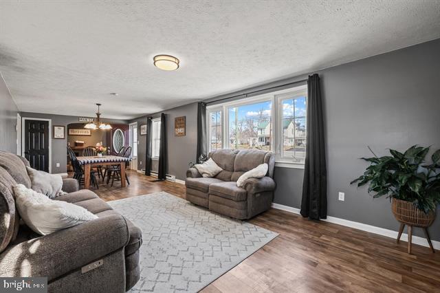 living area with a textured ceiling, baseboards, wood finished floors, and an inviting chandelier