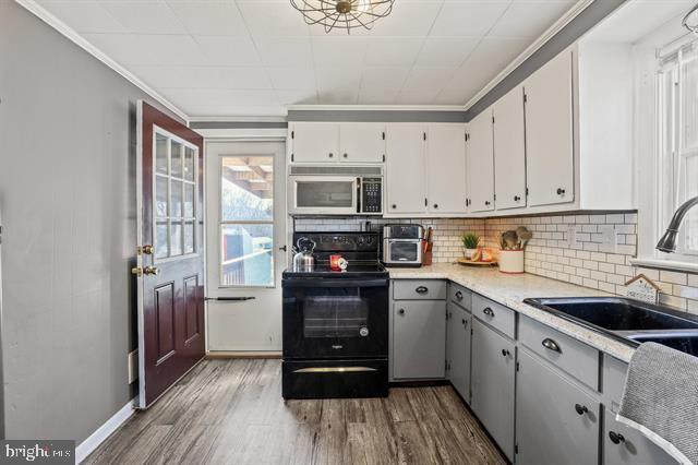 kitchen featuring wood finished floors, electric range, backsplash, and a sink