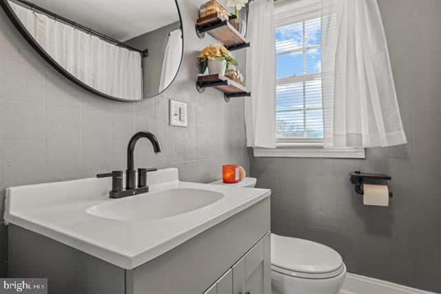 full bathroom with tile walls, toilet, and vanity