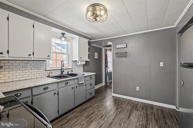 kitchen with dark wood-style floors, backsplash, ornamental molding, a sink, and baseboards