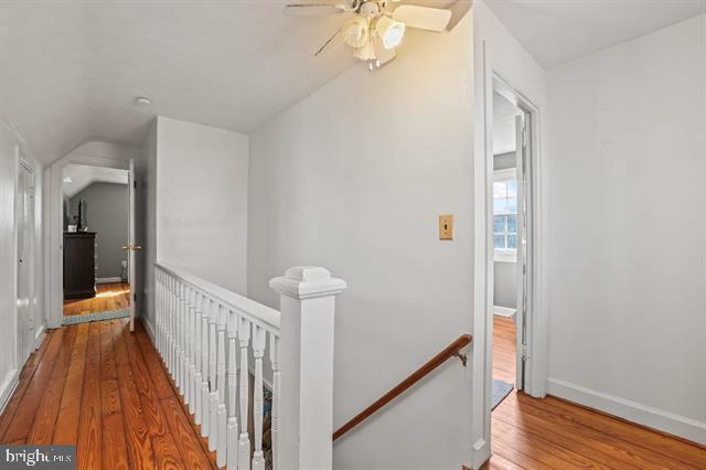 hallway featuring lofted ceiling, baseboards, wood finished floors, and an upstairs landing