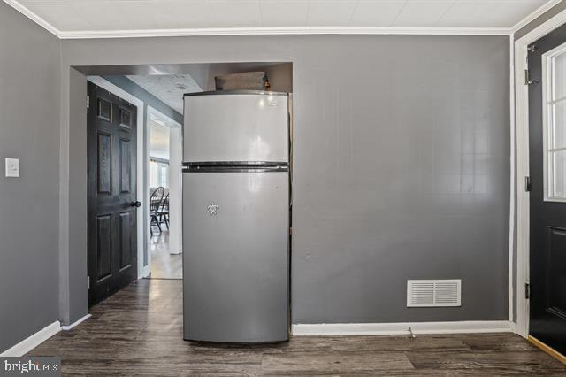 kitchen with baseboards, visible vents, dark wood-style floors, freestanding refrigerator, and crown molding