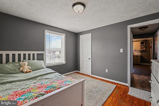 bedroom featuring a textured ceiling, a closet, wood finished floors, and baseboards