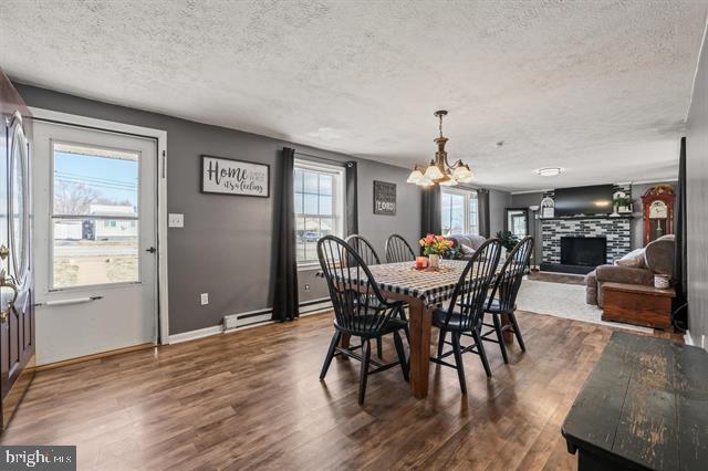 dining area with dark wood-style floors, baseboard heating, a fireplace with raised hearth, and a textured ceiling