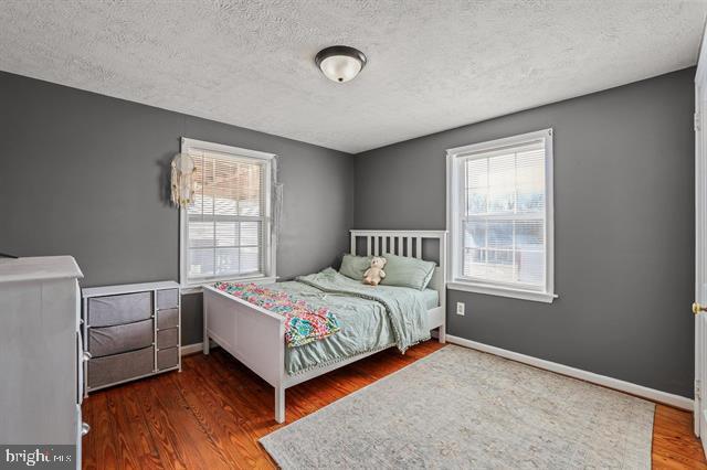 bedroom with a textured ceiling, multiple windows, baseboards, and wood finished floors