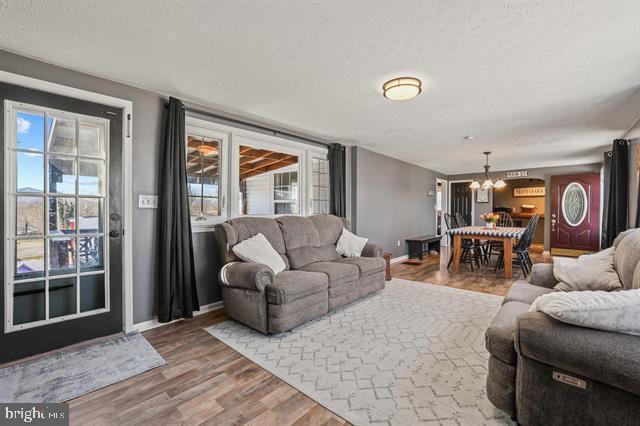 living room with baseboards, a textured ceiling, an inviting chandelier, and wood finished floors