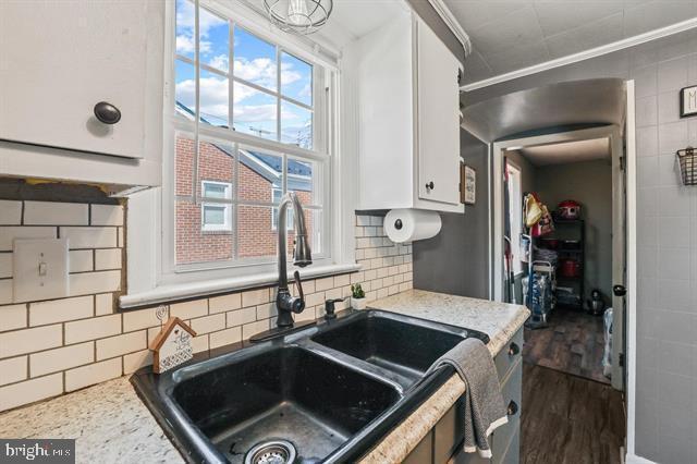 kitchen with dark wood-type flooring, decorative backsplash, white cabinets, and a sink