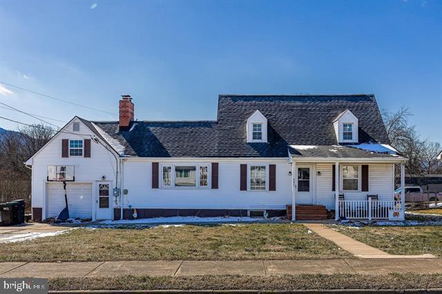 new england style home featuring a garage, covered porch, a chimney, and a front yard