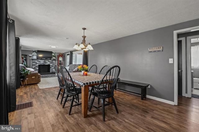 dining space with dark wood-style floors, a fireplace with raised hearth, visible vents, an inviting chandelier, and baseboards