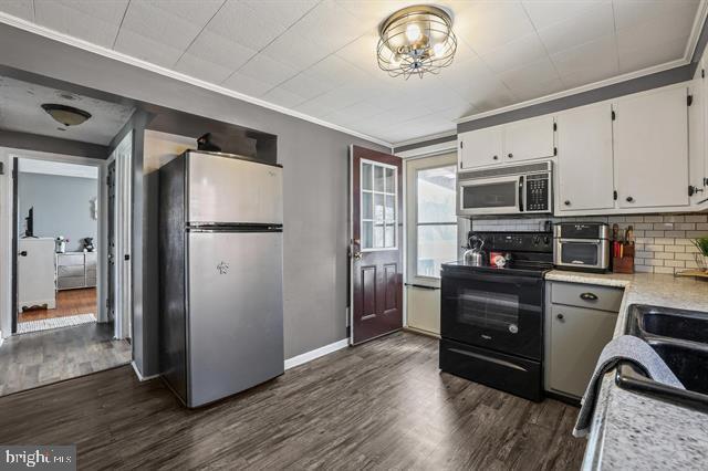 kitchen featuring light countertops, appliances with stainless steel finishes, dark wood-style floors, tasteful backsplash, and crown molding