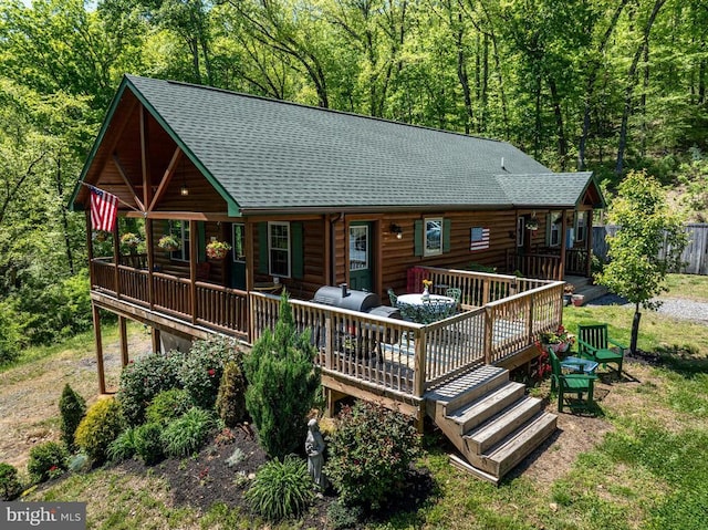 rear view of property with a shingled roof, a deck, and log siding