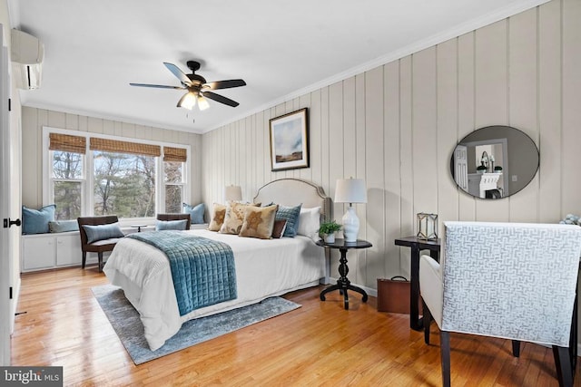 bedroom featuring crown molding, light hardwood / wood-style flooring, a wall unit AC, and ceiling fan