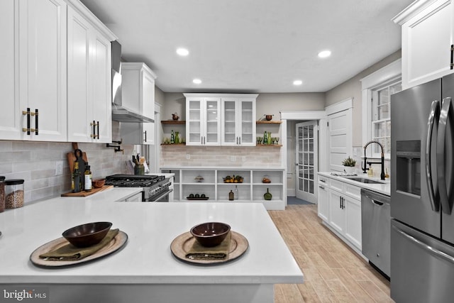 kitchen featuring sink, wall chimney range hood, light hardwood / wood-style flooring, appliances with stainless steel finishes, and white cabinets