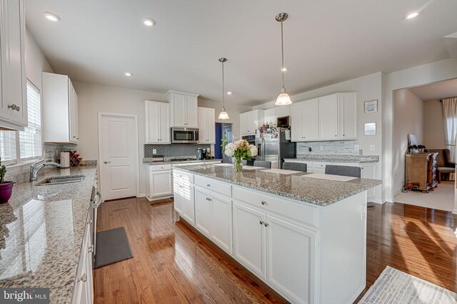 kitchen featuring sink, appliances with stainless steel finishes, white cabinetry, a kitchen island, and decorative light fixtures