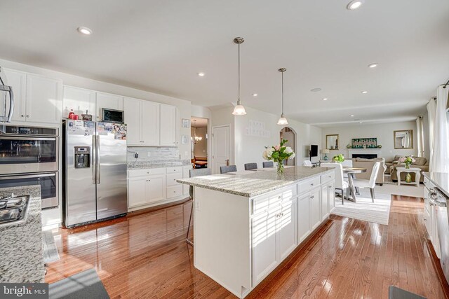 kitchen featuring light stone counters, hanging light fixtures, a kitchen island, stainless steel appliances, and white cabinets