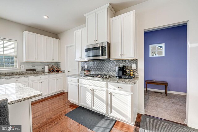 kitchen with appliances with stainless steel finishes, light stone countertops, light wood-type flooring, and white cabinets