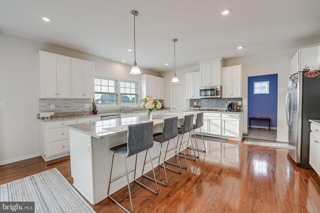 kitchen featuring light hardwood / wood-style flooring, appliances with stainless steel finishes, a center island, light stone counters, and white cabinets