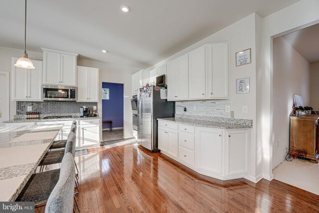 kitchen featuring appliances with stainless steel finishes, decorative light fixtures, white cabinets, light stone counters, and light wood-type flooring