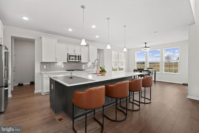 kitchen featuring white cabinets, dark wood finished floors, an island with sink, stainless steel appliances, and backsplash