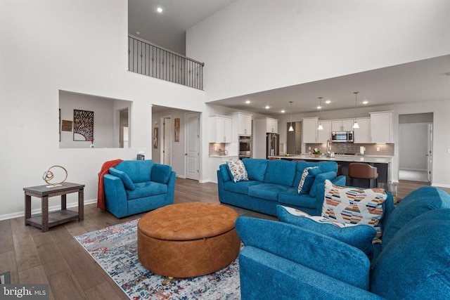 living area featuring recessed lighting, a high ceiling, dark wood finished floors, and baseboards