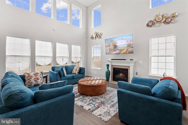 living area featuring a fireplace with flush hearth, a high ceiling, wood finished floors, and baseboards