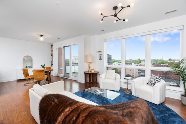living area with baseboards, wood finished floors, visible vents, and a notable chandelier