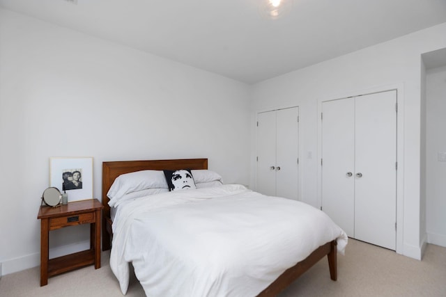 bedroom with light colored carpet, baseboards, and multiple closets