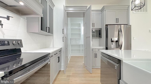 kitchen with decorative light fixtures, light hardwood / wood-style flooring, appliances with stainless steel finishes, custom range hood, and backsplash