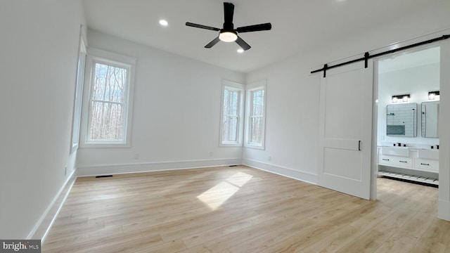 unfurnished bedroom featuring ceiling fan, a barn door, ensuite bath, and light hardwood / wood-style flooring