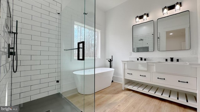 full bathroom featuring double vanity, wood finished floors, a tile shower, a freestanding bath, and a sink