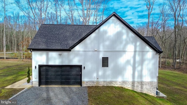 view of side of property with a garage, stone siding, roof with shingles, and a lawn