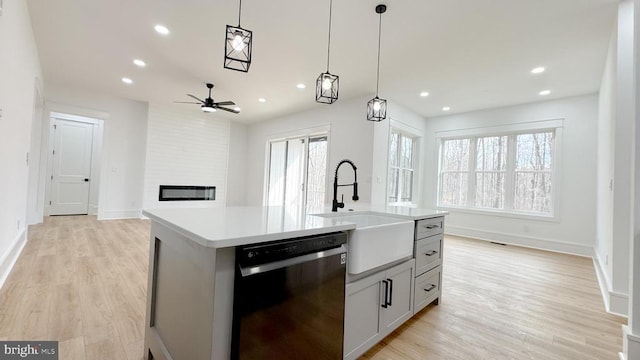 kitchen featuring sink, hanging light fixtures, black dishwasher, a fireplace, and a center island with sink