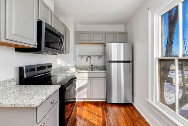 kitchen featuring gray cabinets, hardwood / wood-style floors, sink, stainless steel appliances, and light stone countertops