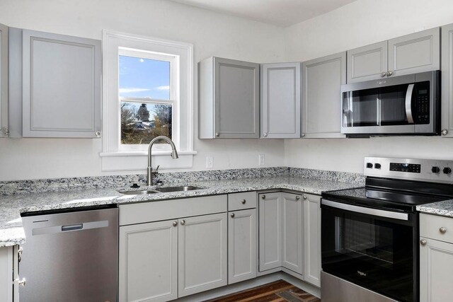 kitchen with light stone counters, sink, stainless steel appliances, and gray cabinetry