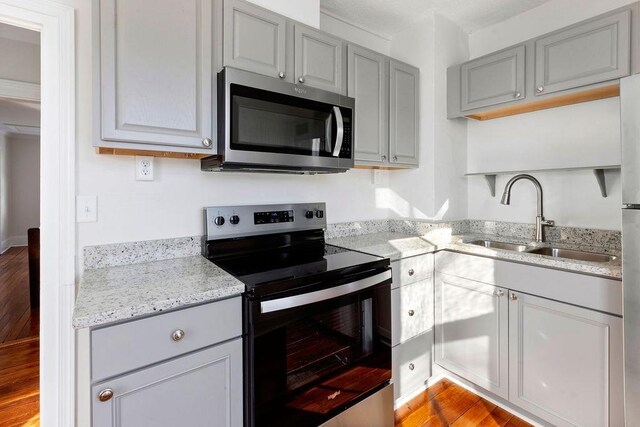 kitchen with sink, light hardwood / wood-style flooring, appliances with stainless steel finishes, gray cabinetry, and light stone counters