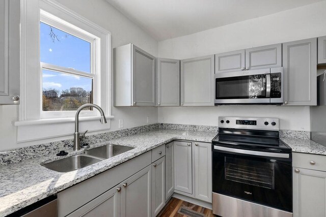 kitchen featuring sink, appliances with stainless steel finishes, gray cabinetry, dark hardwood / wood-style floors, and light stone countertops